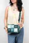 A woman wearing a cream tie-front blouse and blue jeans holds a green and white checkered leather shoulder bag with a braided strap. The brand name 'Kate Spade' is visible on the front of the bag.