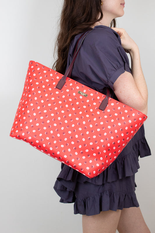 Person holding a red polka dot bag against a plain background