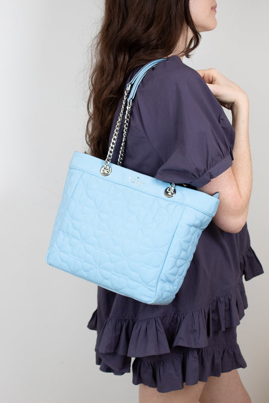 Woman holding a light blue quilted handbag against a plain background