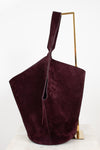 A large, slouchy suede shoulder bag in deep burgundy, displayed on a minimalist gold metal stand against a clean white background.