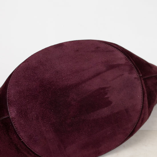A close-up of a deep burgundy suede fabric, showing its soft texture and smooth surface, resting on a light marble surface against a white background.