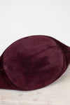 A close-up of a deep burgundy suede fabric, showing its soft texture and smooth surface, resting on a light marble surface against a white background.