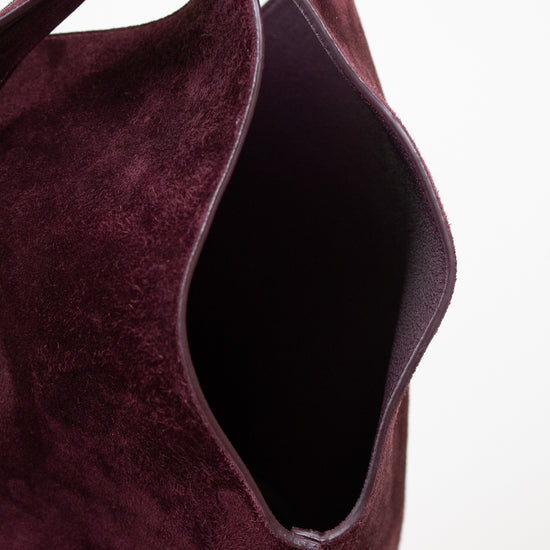 Close-up of a deep burgundy suede shoulder bag, showing the texture of the material and the dark interior, set against a plain white background.
