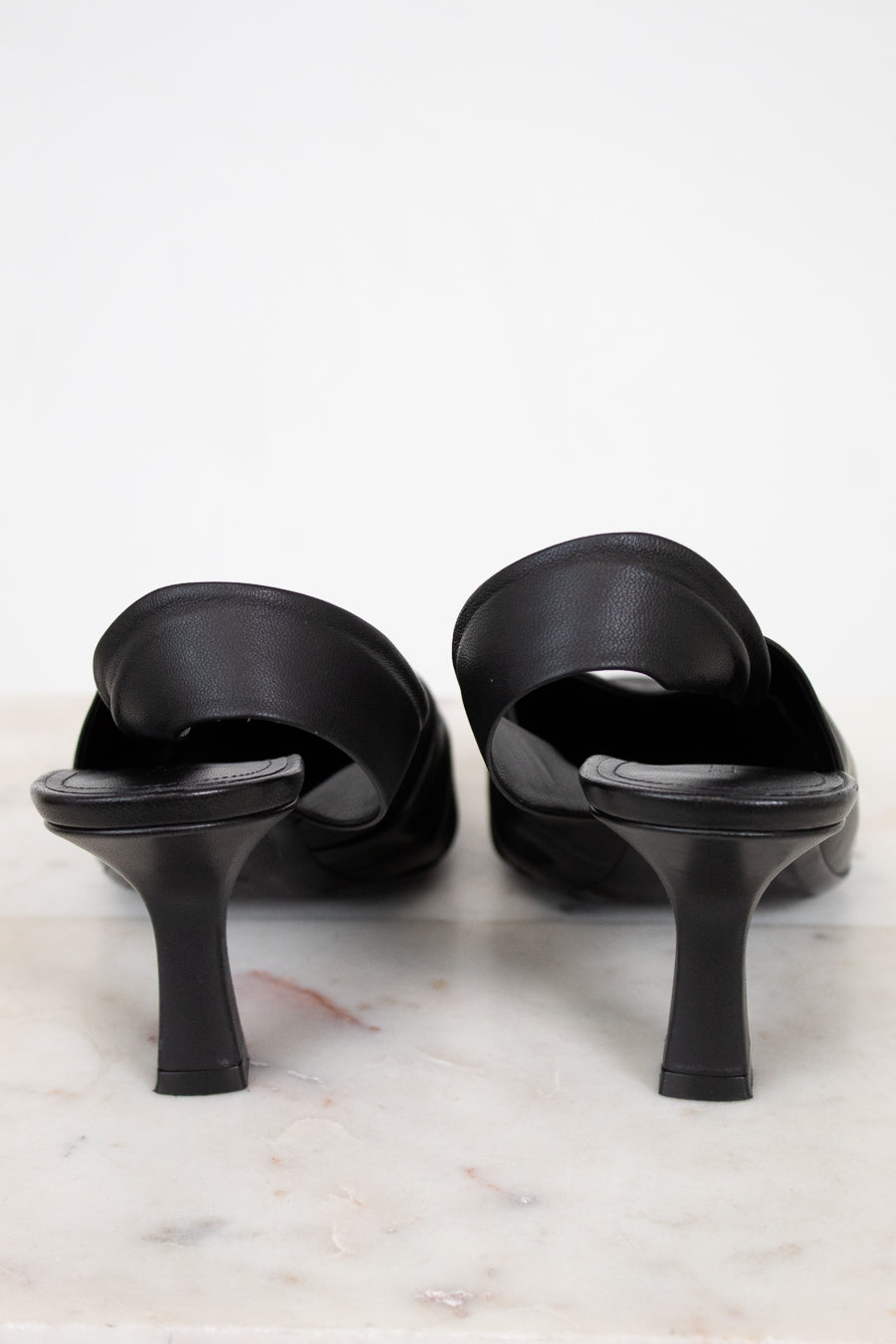 Black high-heeled sandals on a marble surface