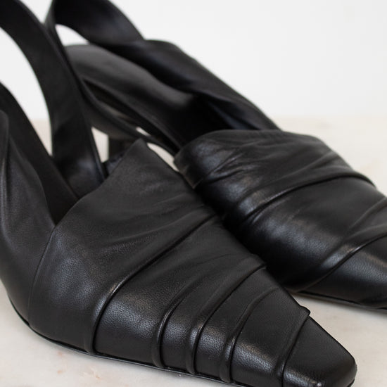 Pair of black leather slingback shoes on a light marble background