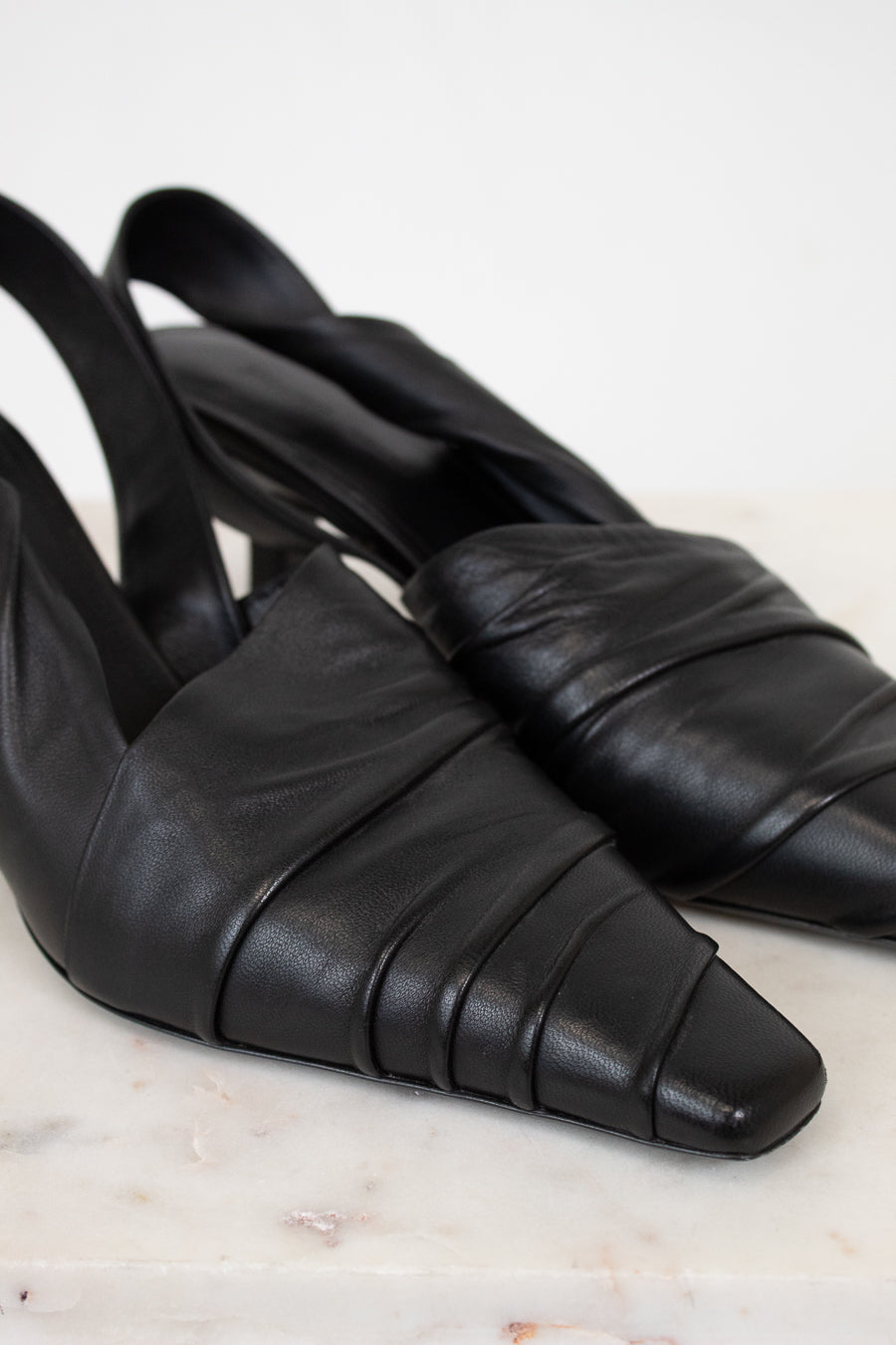 Pair of black leather slingback shoes on a light marble background