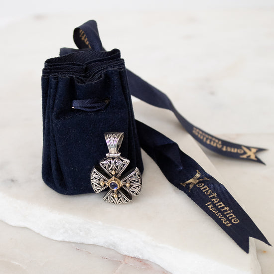 Silver and gold cross pendant leaning on navy dust bag on white marble background