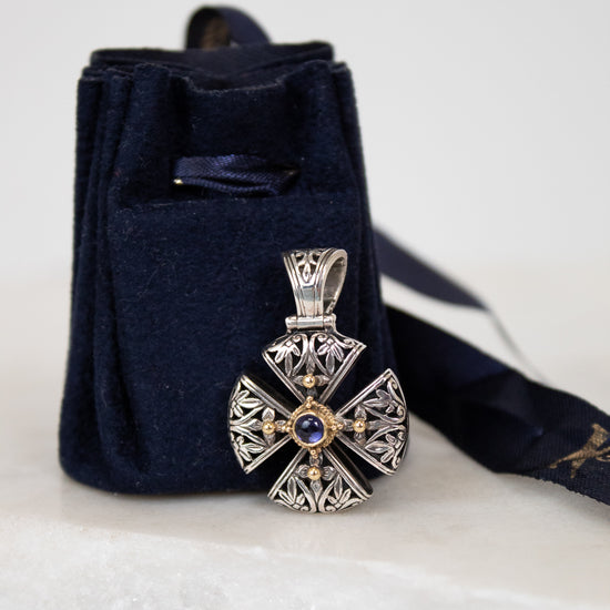 Silver and gold cross pendant leaning on navy dust bag on white marble background