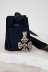 Silver and gold cross pendant leaning on navy dust bag on white marble background
