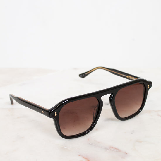 Black sunglasses with brown lenses on a light marble surface