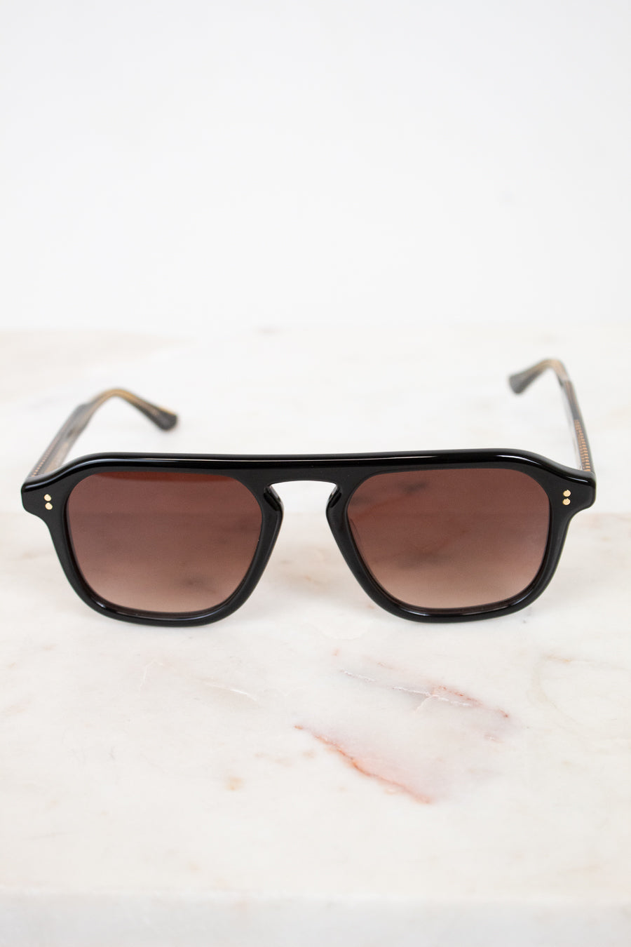 Black sunglasses with brown lenses on a light marble background
