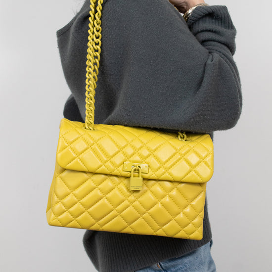 Person wearing a yellow quilted handbag with a chain strap on a plain background