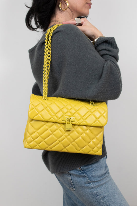 Person wearing a yellow quilted handbag with a chain strap on a plain background