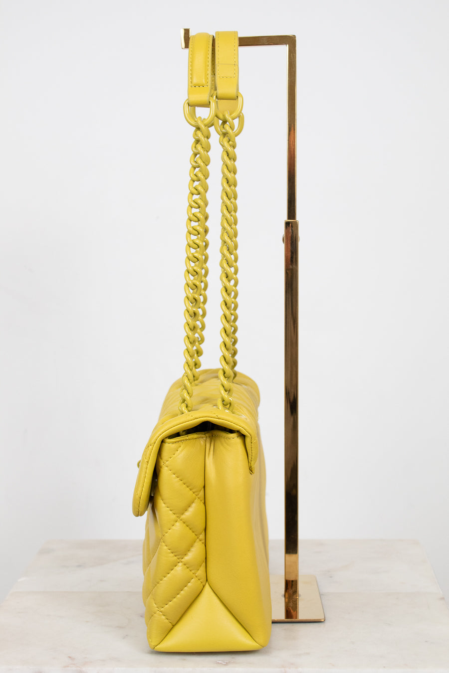 Yellow quilted handbag with yellow chain strap on a white background