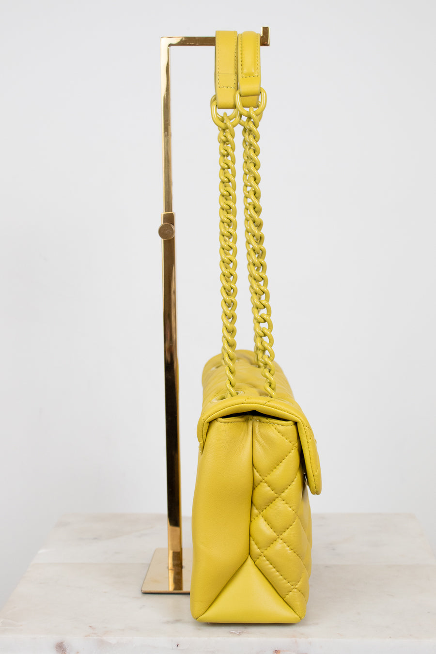 Yellow quilted handbag with a yellow chain on a white background
