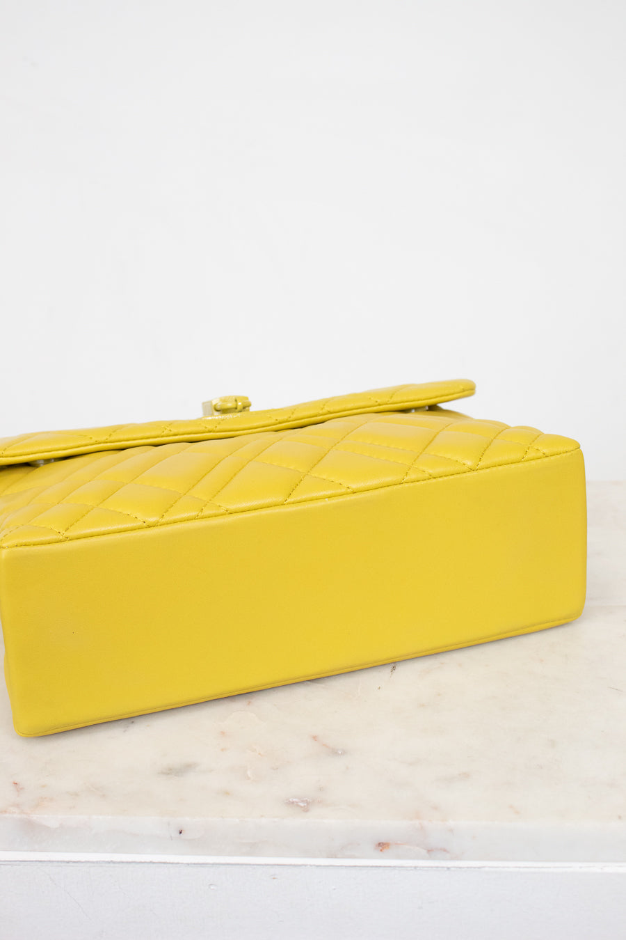 Yellow quilted handbag on a light marble surface with a white background