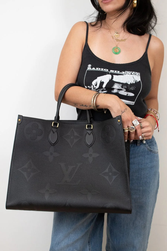 Person holding a black handbag with a visible brand logo, wearing a black tank top and blue jeans.