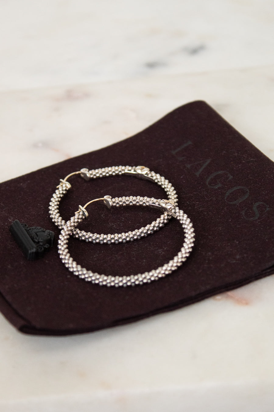 Silver hoops rested on brown dustbag on white background