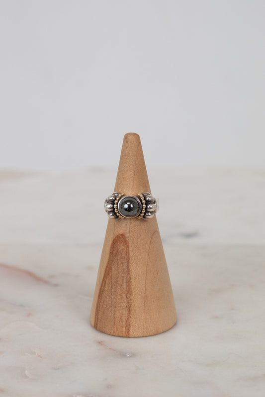 Silver ring with a dark stone on a wooden cone against a light background