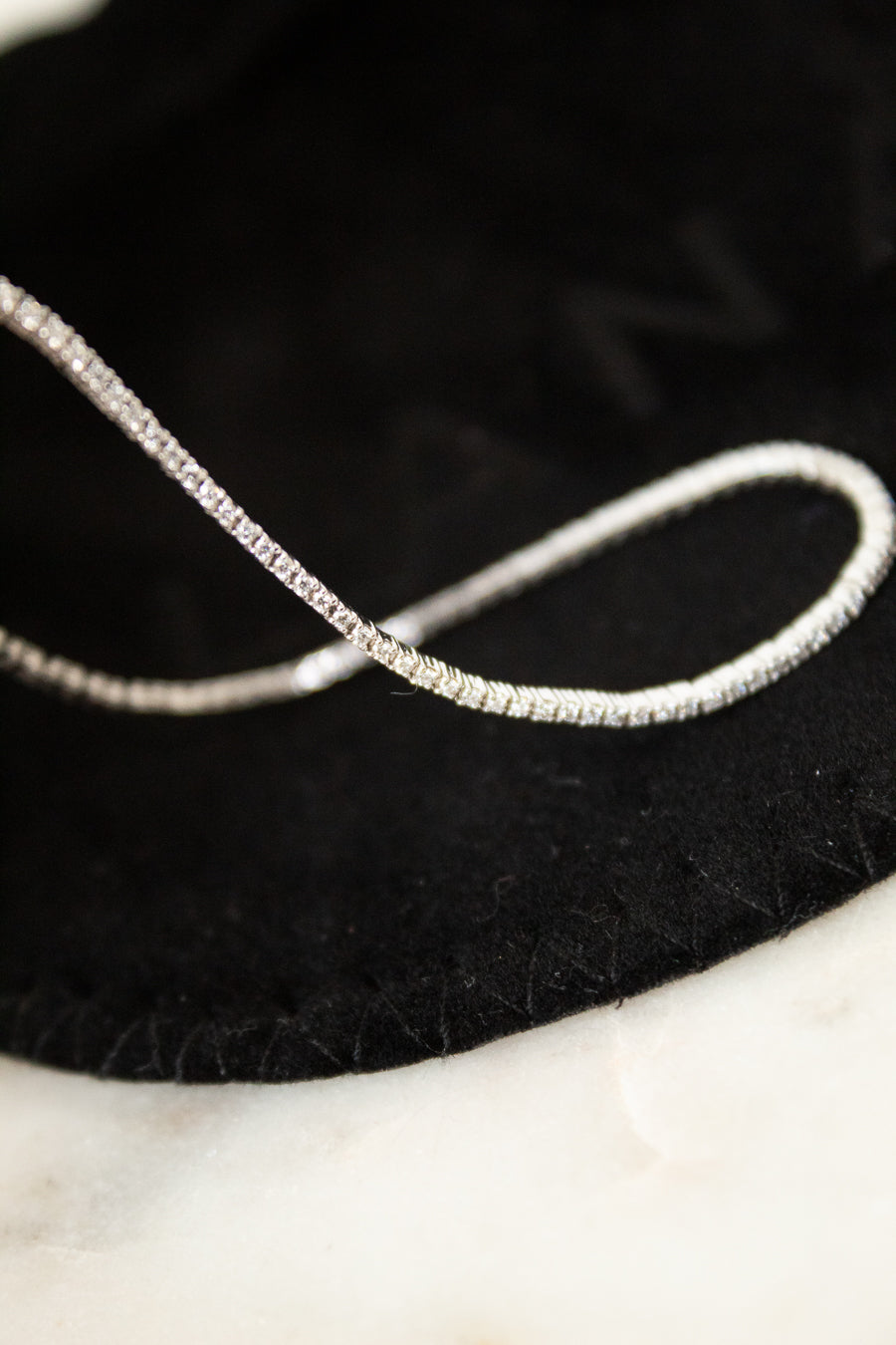 Silver and diamond bracelet on a black dust bag with a marble surface