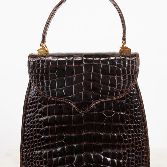 A dark brown alligator leather handbag with a top handle and gold-tone hardware, photographed against a clean white background.