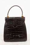 A dark brown alligator leather handbag with a top handle and gold-tone hardware, photographed against a clean white background.