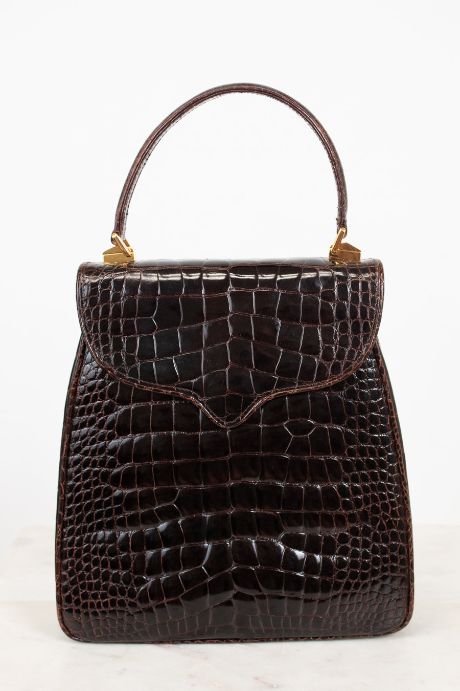 A dark brown alligator leather handbag with a top handle and gold-tone hardware, photographed against a clean white background.