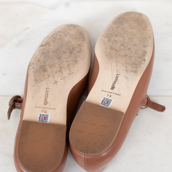 Brown shoes with visible wear to bottom soles on a white surface