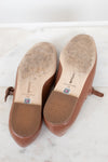 Brown shoes with visible wear to bottom soles on a white surface