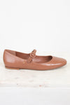 Brown leather flat shoe with a round buckle on a light marble surface.
