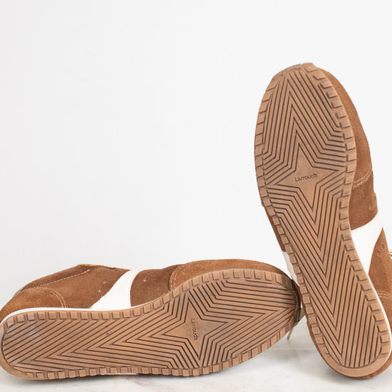 A pair of brown suede slip-on shoes shown from the bottom, with one shoe standing upright to display the treaded sole and the other lying flat to show the side profile, set against a clean white background.