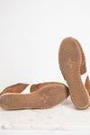 A pair of brown suede slip-on shoes shown from the bottom, with one shoe standing upright to display the treaded sole and the other lying flat to show the side profile, set against a clean white background.