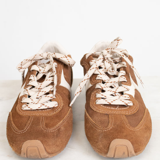 A pair of vintage-style brown suede sneakers with white side stripes and chunky cream rope laces, shown from the front on a light marble surface against a white background.