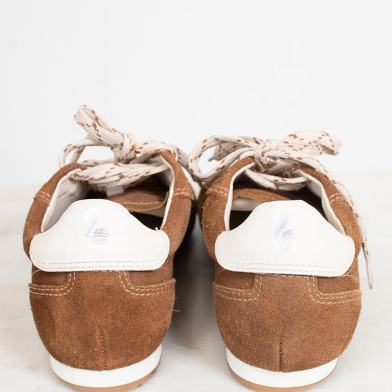 A pair of brown suede low-top sneakers shown from the back, featuring white heel tabs and cream-colored laces, set against a light gray background.