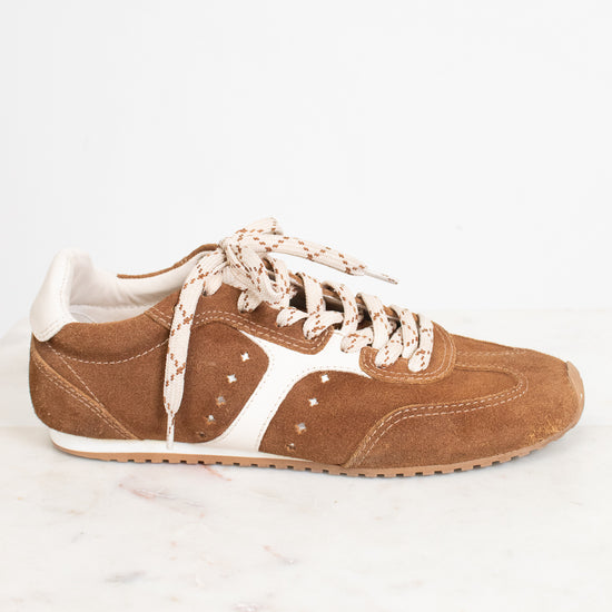 A single brown suede sneaker with cream-colored laces and side stripes, displayed on a white marble surface against a white background.
