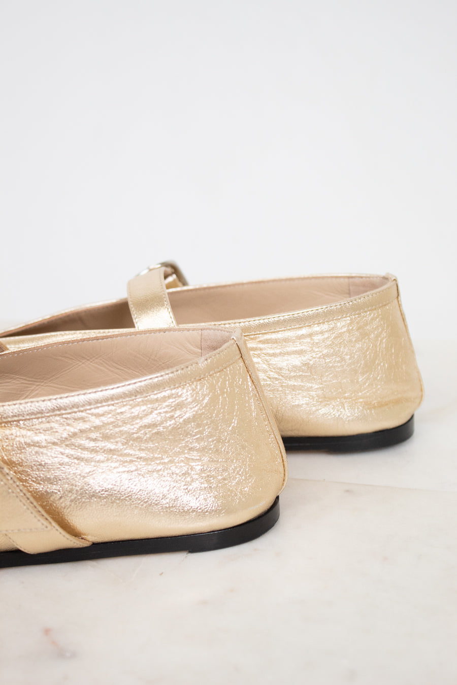 Pair of gold metallic flats on a white background