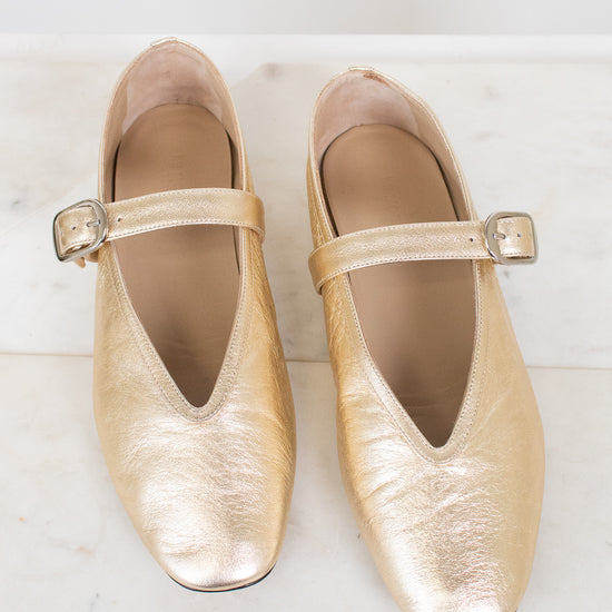 Pair of gold metallic shoes with squared almond toes on a light marble background