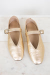 Pair of gold metallic shoes with squared almond toes on a light marble background
