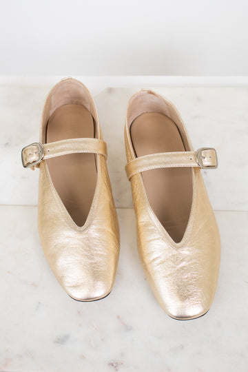 Pair of gold metallic shoes with squared almond toes on a light marble background