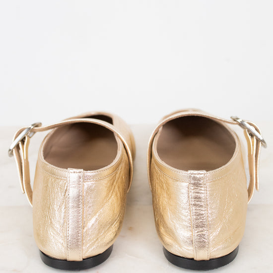 Pair of gold flat shoes on a light marble background