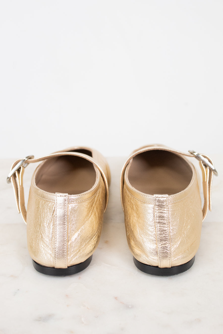 Pair of gold flat shoes on a light marble background