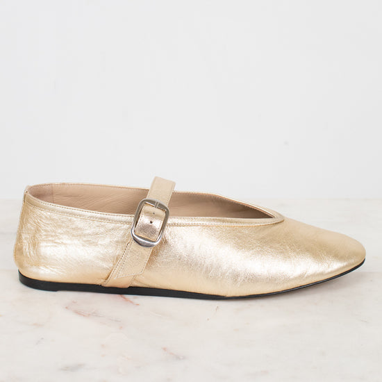 Gold metallic flat shoe with a strap on a light background