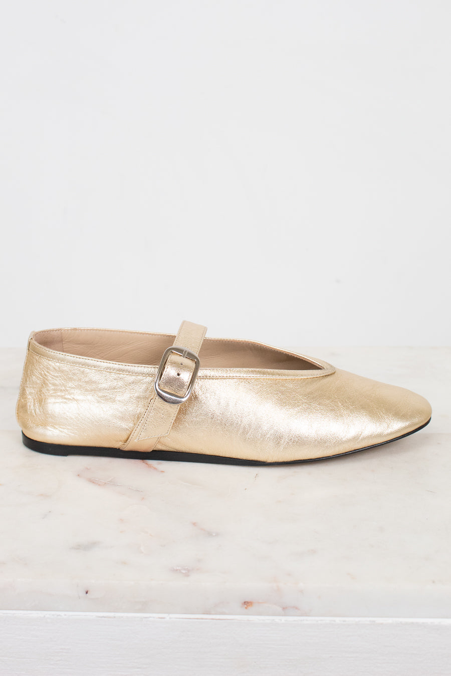 Gold metallic flat shoe with a strap on a light background