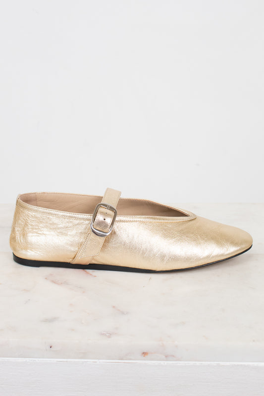 Gold metallic flat shoe with a strap on a light background