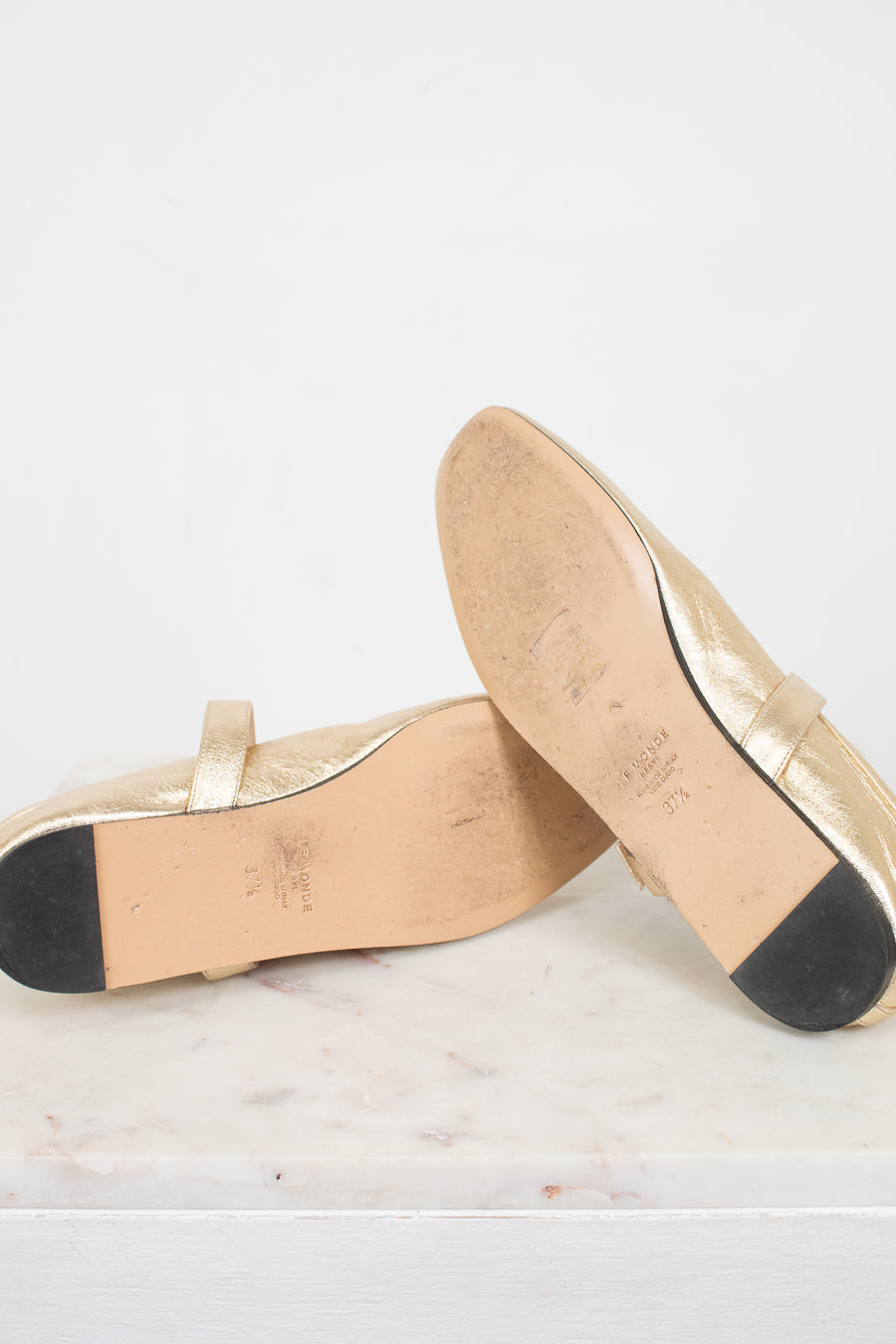 Bottom soles of gold shoes on a white marble surface
