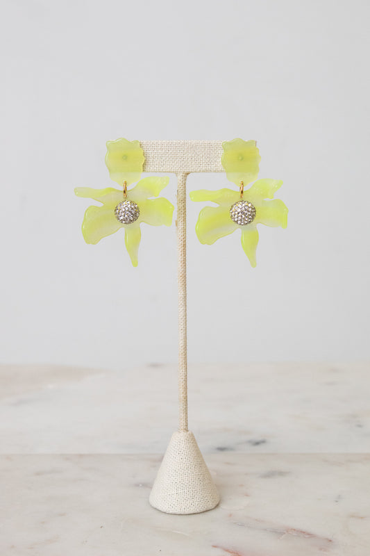 A pair of yellow-green flower-shaped earrings with a textured silver center, displayed on a beige woven jewelry stand against a light gray background.