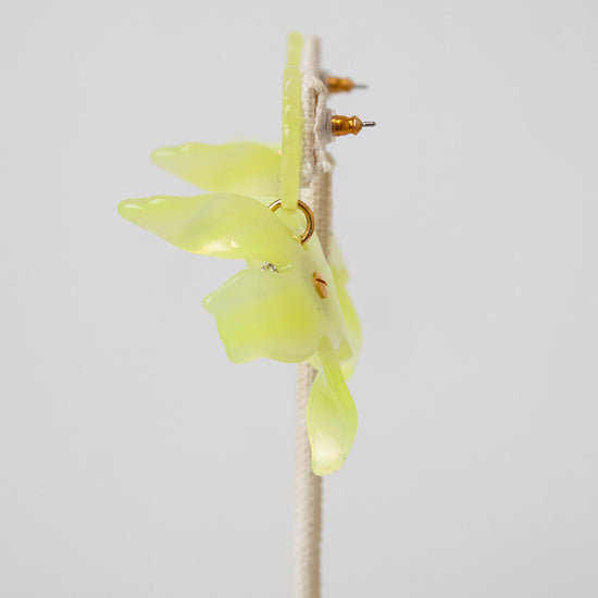 A yellow-green translucent acetate flower with small gold details, mounted on a beige wire stand against a plain light gray background.