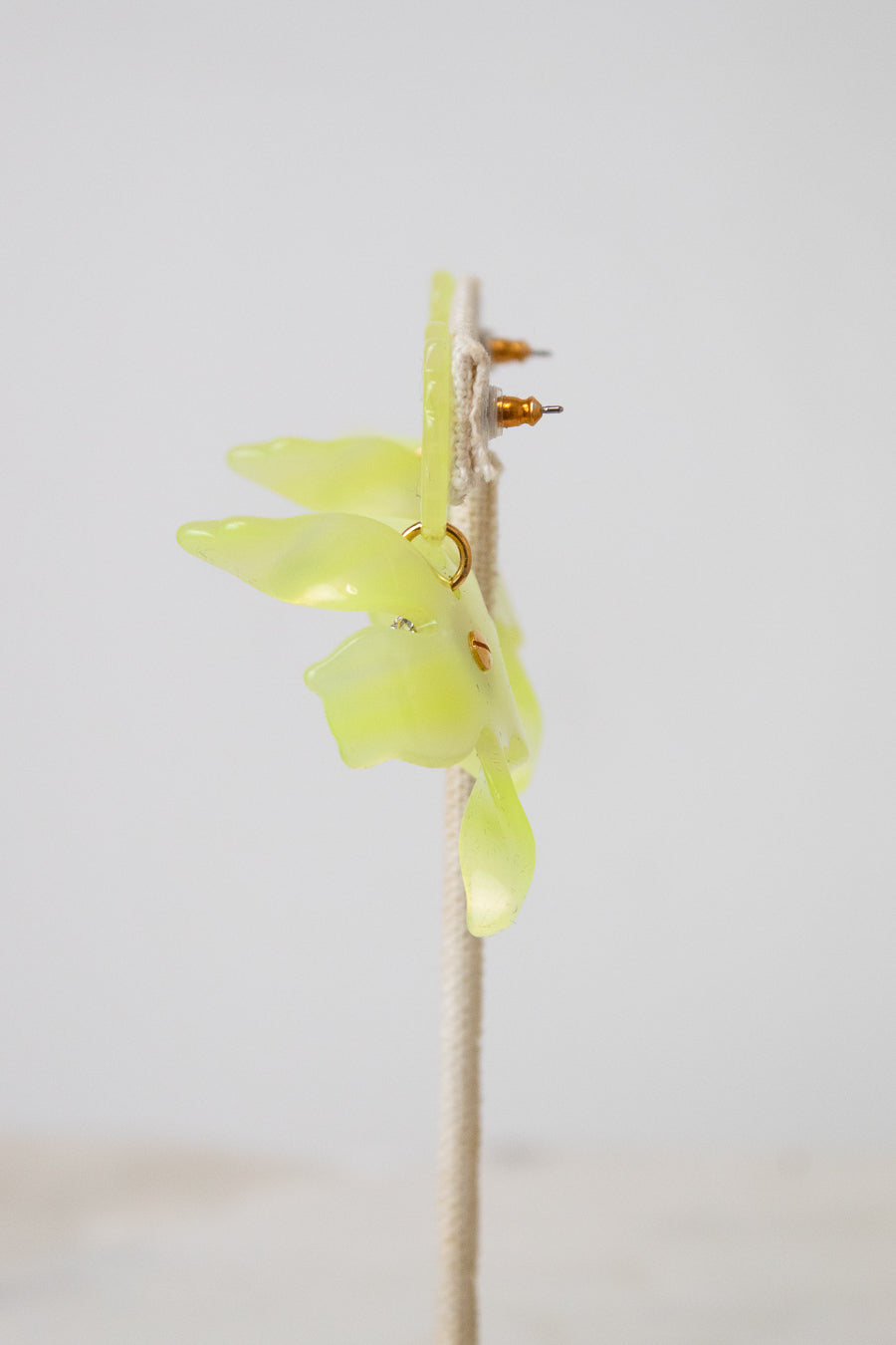A yellow-green translucent acetate flower with small gold details, mounted on a beige wire stand against a plain light gray background.