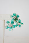 A pair of turquoise and green marbled flower-shaped earrings with clear rhinestone centers, displayed on a cream-colored jewelry stand against a light gray background.