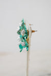 A pair of floral earrings with translucent green glass petals, clear rhinestone clusters, and gold-tone metal posts, displayed on a white stand against a light gray background.